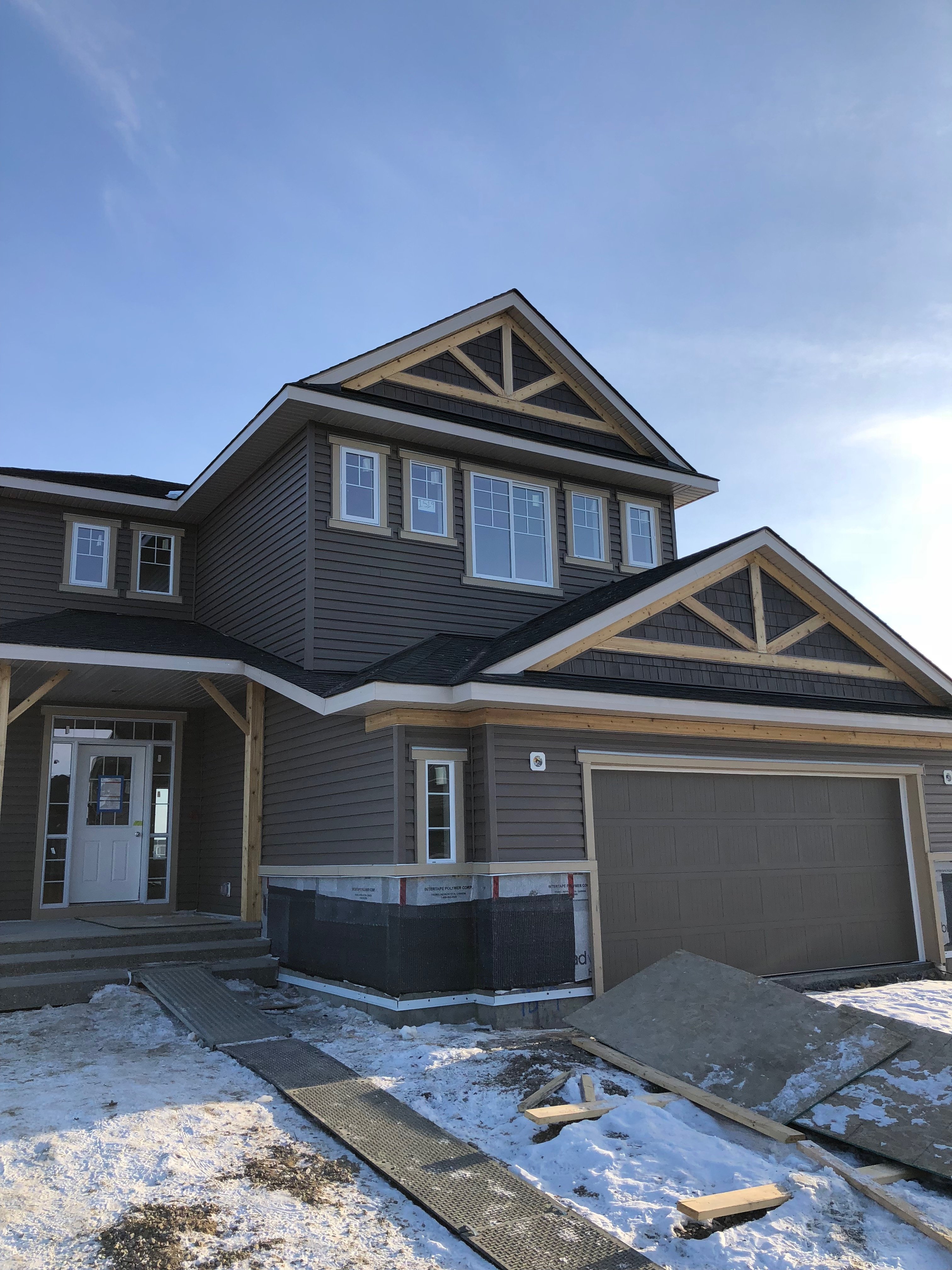Two-story house under construction with a gable roof and garage, set against a clear blue sky.